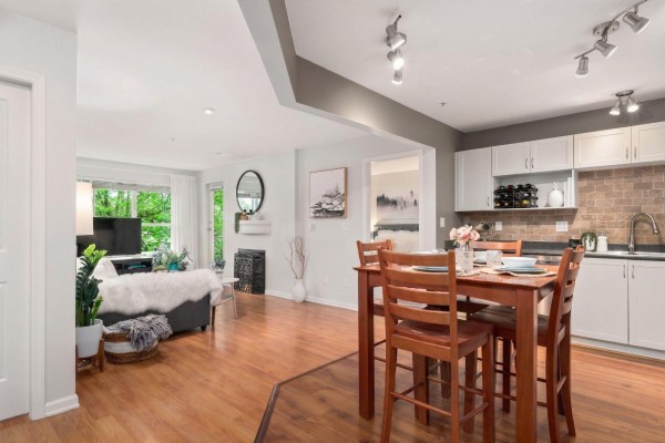 Apartment open concept living and dining area with kitchen, wood floors, and wooden dining table. - 311 10188 155 Street, Surrey