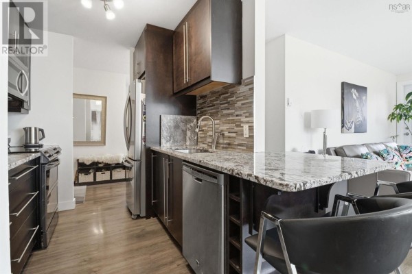 Interior kitchen view with dark wood cabinets, granite countertops, stainless steel appliances, and view into living area. - 311-41 Moirs Mill Road, Bedford
