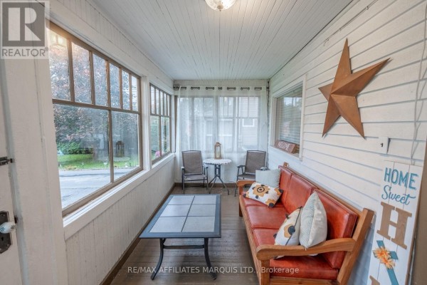Screened-in porch with wood-paneled walls, a wooden sofa, and two chairs. - 311 Fourth Street W, Cornwall