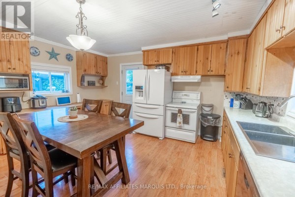 Kitchen interior with wood cabinetry, white appliances, a sink, and a wooden dining set. - 311 Fourth Street W, Cornwall