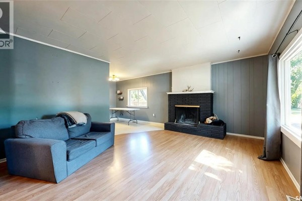 Spacious living room with a blue sofa, black brick fireplace, light wood floors, and large windows. - 311 Pottery Street, Eastend