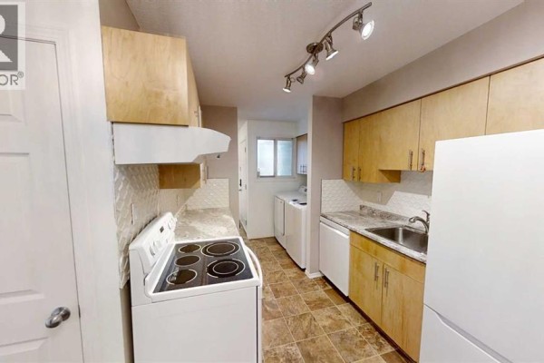 Kitchenette with light wood cabinets, speckled countertops, white appliances, and tiled floor. - 3110, 7201 Poplar Drive, Grande Prairie