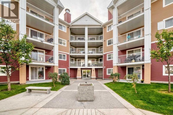 Building courtyard with paved walkway, grass, bench, and central planter. - 3116, 10 Prestwick Bay Se, Calgary