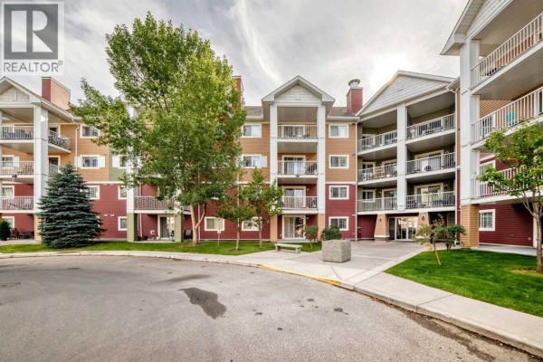 Apartment building exterior with red and tan siding, balconies, and trees. - 3116, 10 Prestwick Bay Se, Calgary