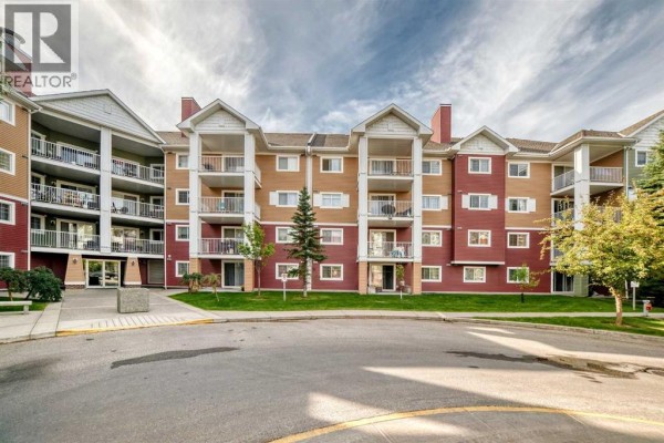 Apartment building exterior with red and tan siding, balconies, and green lawn. - 3116, 10 Prestwick Bay Se, Calgary