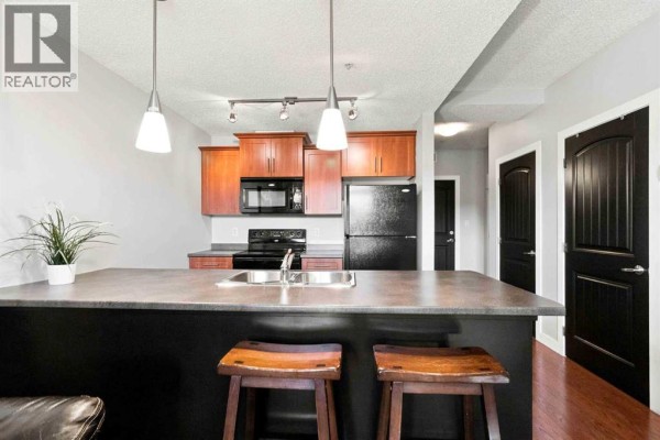 Kitchen island with bar stools, wood cabinets, black appliances, and doorway access. - 3117, 135c Sandpiper Road, Fort Mcmurray