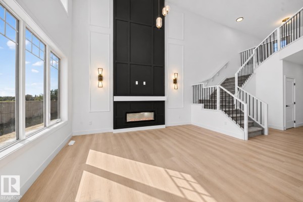 Empty living room featuring light wood floors, a modern fireplace, and large windows. - 3119 9 St Nw, Edmonton