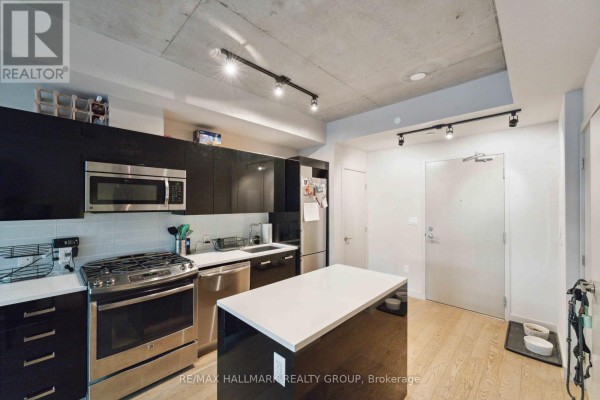 Modern kitchen with stainless steel appliances, black cabinetry, and a white island. - 312 - 224 Lyon Street N, Ottawa