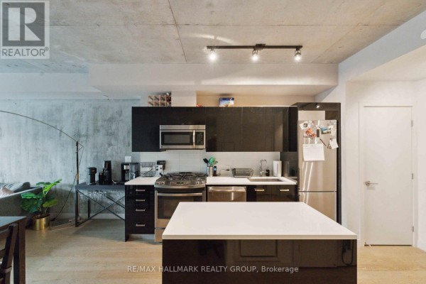 Open concept kitchen and living area with concrete walls and black cabinetry. - 312 - 224 Lyon Street N, Ottawa