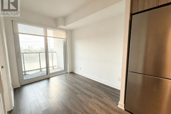 Apartment living area with a sliding glass door to balcony, and stainless steel refrigerator. - 312 - 30 Samuel Wood Way, Toronto