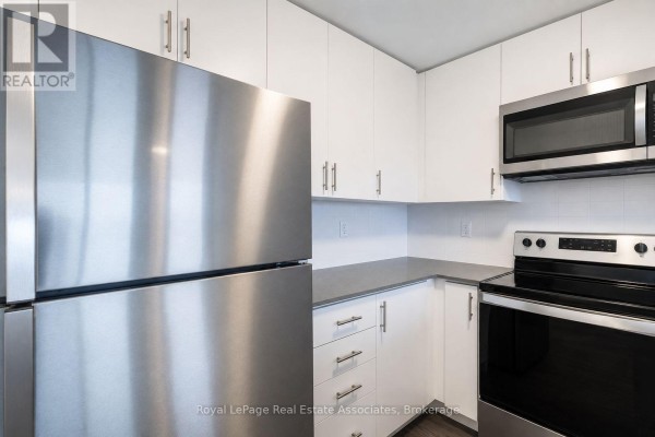 Empty living room with white walls, dark wood floors, and large windows. - 312 - 3401 Ridgeway Drive, Mississauga