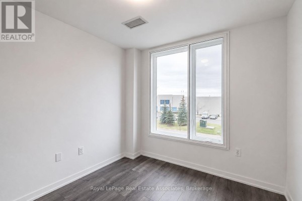 Bedroom with white walls, dark wood floors, and a large corner window. - 312 - 3401 Ridgeway Drive, Mississauga