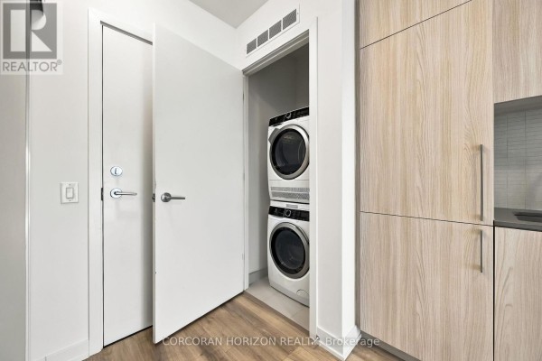 Closet with stacked white washer and dryer, next to apartment entrance. - 312 - 7437 Kingston Road, Toronto