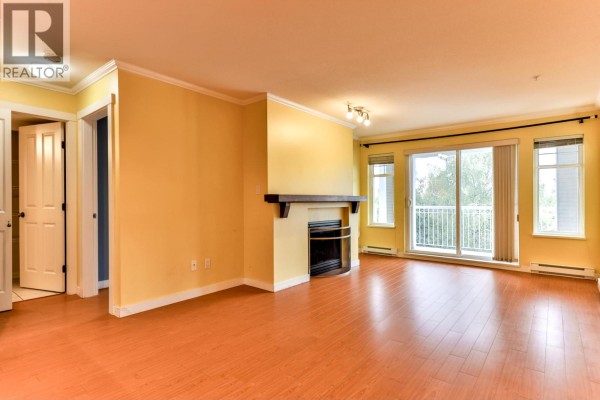 Living room with yellow walls, hardwood floors, fireplace, and balcony access through sliding glass doors. - 312 1420 Parkway Boulevard, Coquitlam