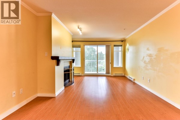Living room with yellow walls, hardwood floors, fireplace, and balcony access with sliding glass doors. - 312 1420 Parkway Boulevard, Coquitlam