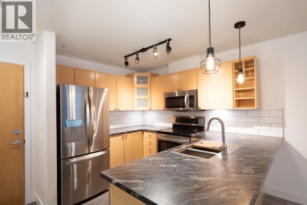 Dining area and living room with a large window, sofa, and houseplants. - 312 3136 St Johns Street, Port Moody