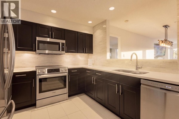 L-shaped kitchen with dark wood cabinets, stainless steel appliances including a Bosch range, and white quartz countertops. - 312 3480 Main Street, Vancouver