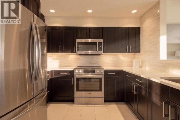 Corner kitchen with dark wood cabinets, stainless steel appliances, and a tiled backsplash, viewed from the side. - 312 3480 Main Street, Vancouver