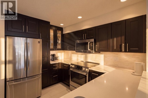 Kitchen area showing dark wood cabinets, stainless steel appliances, a built-in wine rack, and white quartz countertops. - 312 3480 Main Street, Vancouver