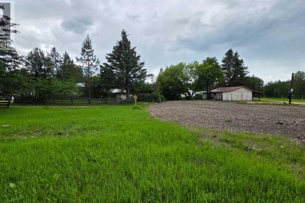 Open grassy area adjacent to a gravel lot with a fence, trees, and a detached building. - 312 3rd Street, Blue Ridge