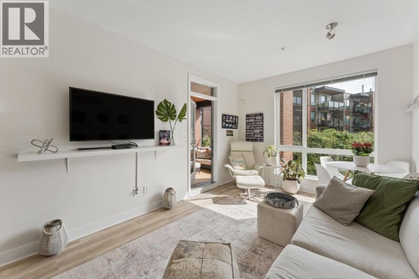 Living and dining area with sofa, small white table, chairs, and kitchen counter with stools. - 312 733 W 3rd Street, North Vancouver