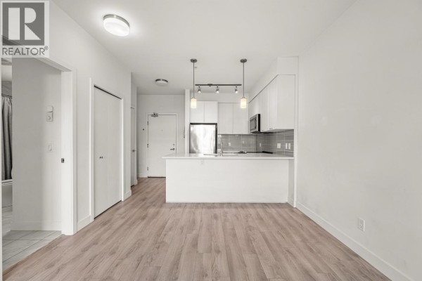 Open-concept apartment interior showing a kitchen with white cabinets and stainless steel appliances, adjacent to a living area. - 312 828 Gauthier Avenue, Coquitlam
