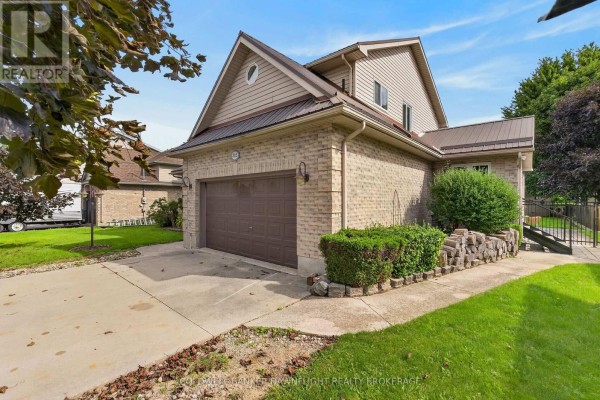 View of the side of a beige brick house with a brown garage door and a manicured lawn. - 312 Beech Street, Lucan Biddulph