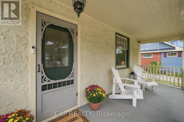 Close-up of a covered front porch with two Adirondack chairs, a screen door, and flower pots. - 312 Walnut Street W, Whitby