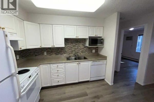 U-shaped kitchen with white cabinets, stainless steel sink, microwave, dishwasher, and a view of another room. - 3120, 3000 Millrise Point Sw, Calgary