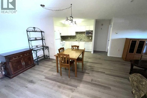 View of the dining area and kitchen from the living room, featuring wood furniture and light-colored flooring. - 3120, 3000 Millrise Point Sw, Calgary