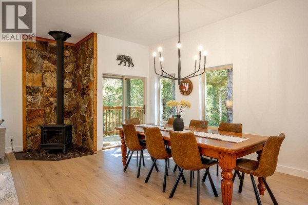 Dining area with large wooden table, chairs, and a stone-clad wood-burning stove. - 3125 Hawthorne Place, Whistler