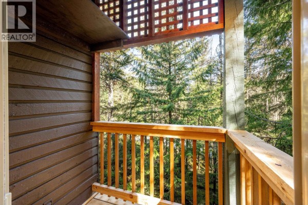 Wooden balcony railing and lattice detail with a view of evergreen trees. - 3125 Hawthorne Place, Whistler