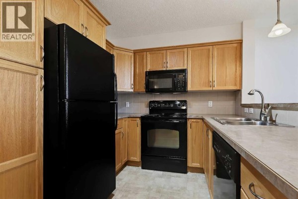Kitchen with light oak cabinets, black refrigerator, black stove, and beige countertops. - 313, 380 Marina Drive, Chestermere