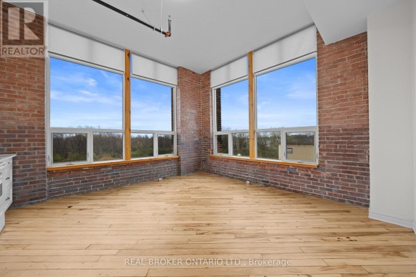 Corner room with large windows, exposed brick walls, and light wood floors. - 313 - 150 Mill Street, Carleton Place