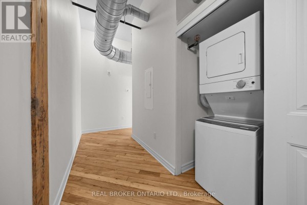 Hallway with exposed pipes, laundry machines, and light wood floors. - 313 - 150 Mill Street, Carleton Place