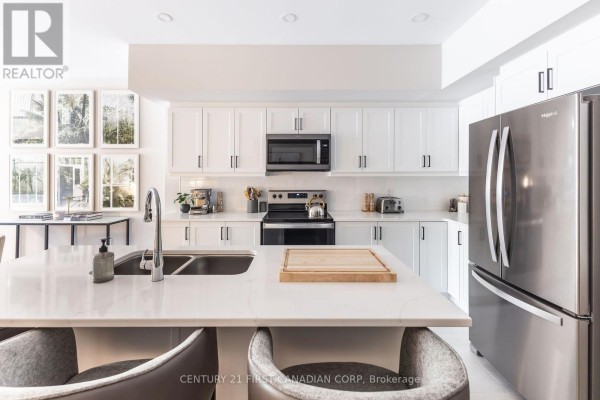 Modern white kitchen with stainless steel appliances and quartz countertops. - 313 - 230 North Centre Road, London North