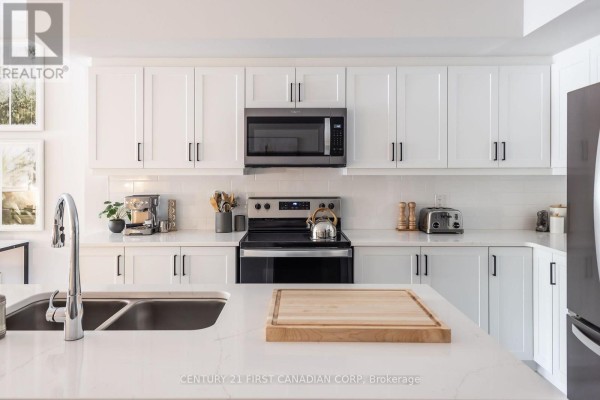 Close-up of a white kitchen with stainless steel appliances and quartz island. - 313 - 230 North Centre Road, London North