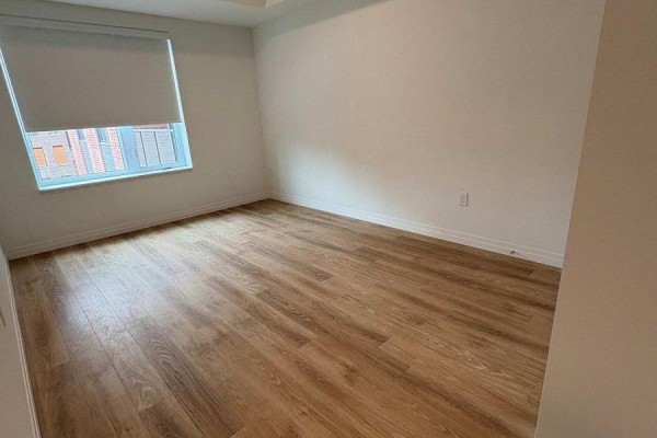Empty room with light wood laminate flooring, white walls, and a large window. - 313 - 351 Hill Street, London East