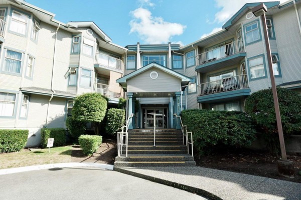 Front entrance of an apartment building with a set of stairs and manicured bushes. - 313 10756 138 Street, Surrey