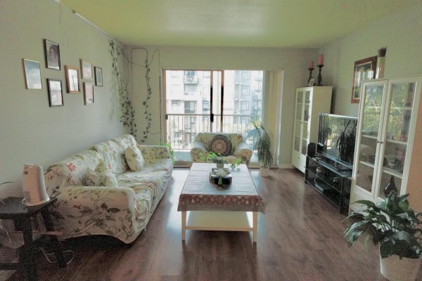 Living room with a floral sofa, coffee table, television, and large window overlooking buildings. - 313 10756 138 Street, Surrey