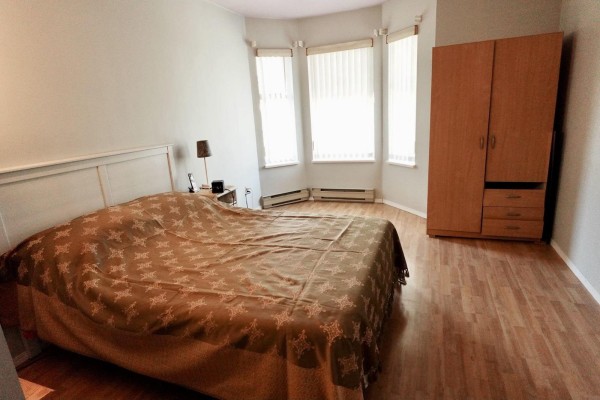 Bedroom with a large bed, bay windows, and a wooden wardrobe. - 313 10756 138 Street, Surrey