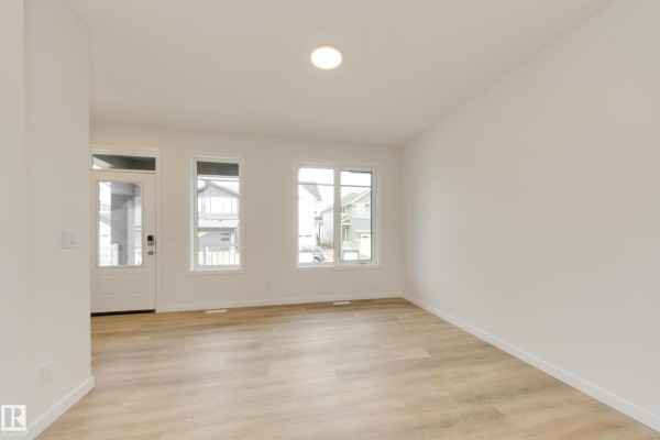 Bright living room with white walls, light wood floors, and two windows overlooking the street. - 313 173 Av Nw, Edmonton