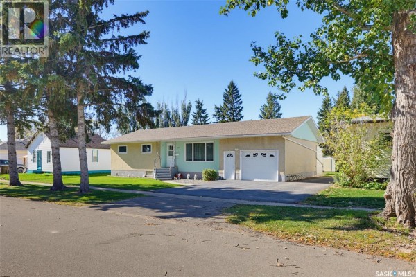 Side exterior view of a bungalow with a light yellow facade, attached garage, and a driveway. - 313 4th Avenue, Cudworth