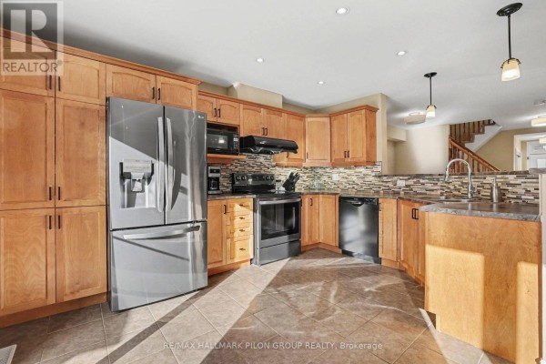Spacious kitchen with light wood cabinets, stainless steel refrigerator, black appliances, and tiled flooring. - 3130 Burritts Rapids Place, Ottawa
