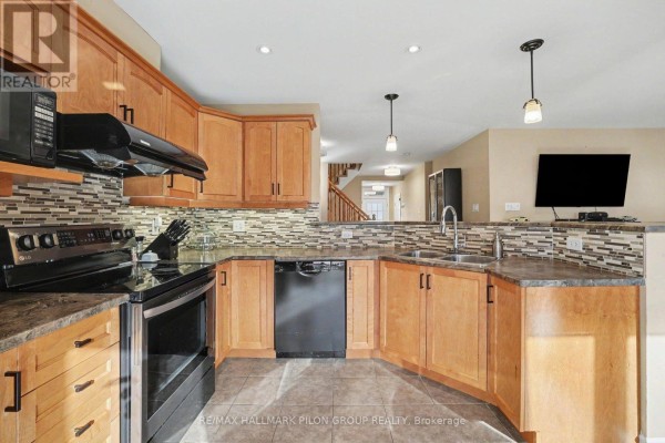 Kitchen with light wood cabinets, black appliances, stainless steel sink, and view of dining area stairs. - 3130 Burritts Rapids Place, Ottawa