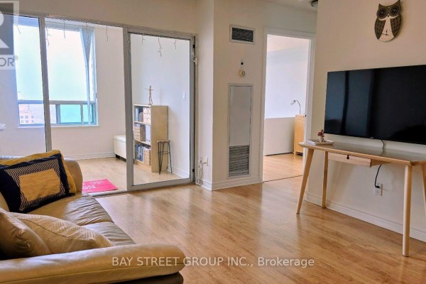 Living room with leather couch, TV, and doorway to sunroom with bookshelf. - 3131 - 68 Corporate Drive, Toronto