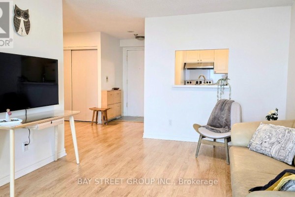 Living room with couch, TV, and view into kitchen area with pass-through. - 3131 - 68 Corporate Drive, Toronto