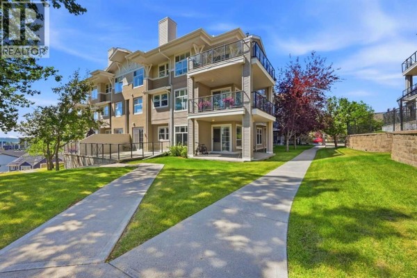 Apartment building exterior with grass, walkways, and trees under a blue sky. - 3137, 1010 Arbour Lake Road Nw, Calgary