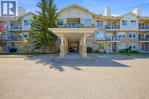 Apartment building entrance with covered canopy and parking lot. - 3137, 1010 Arbour Lake Road Nw, Calgary