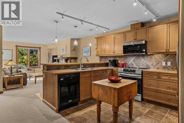 Open-concept living and kitchen area with a fireplace, sofa, and a wooden butcher block island. - 314, 170 Crossbow Place, Canmore